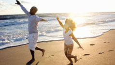 Two people running on the beach with their arms spread out with footprints and a sunset in the background.
